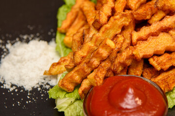 French fries in ketchup. Two slices of potatoes in sauce on a lettuce leaf. Black background.