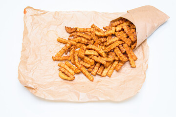 Fried crispy French fries in a paper bag. The potatoes are scattered over the paper. Fast food. Isolated on white background