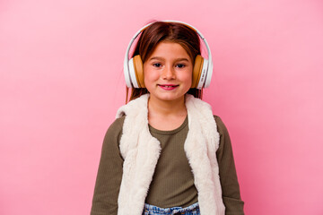 Little caucasian girl listening music isolated on pink background happy, smiling and cheerful.