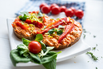 vegan roasted red pepper dip sandwich spread on freshly baked bread slice with salad garnish on white porcelain plate 