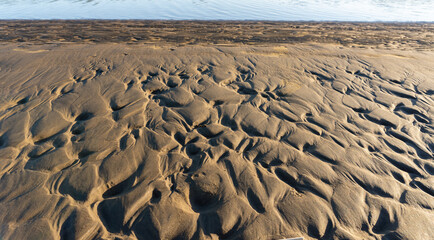 Wavelets formed on the sand and silty-clay shore. Pattern. Brown and gold colors. Sand patterns on the beach at low tide. La Plata River, Atalaya, Buenos Aires. La Plata River.