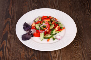 Fresh vegetable salad with onions and basil on a white plate