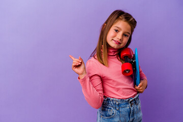 Little skater caucasian girl isolated on blue background smiling and pointing aside, showing something at blank space.