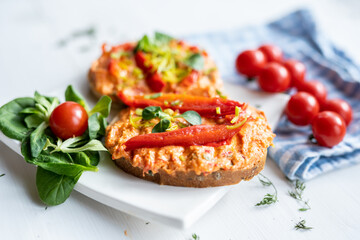 vegan roasted red pepper dip sandwich spread on freshly baked bread slice with salad garnish on white porcelain plate 
