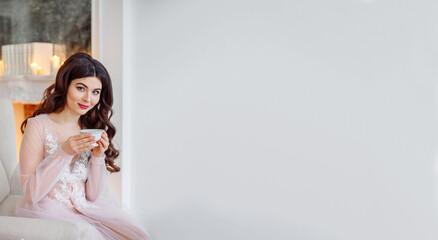 Morning of the bride. She is in a white interior drinking tea. Beautiful curls and wedding makeup