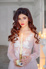 Portrait of a bride in a white interior in a beautiful boudoir semi-transparent dress. She holds a candle in her hand