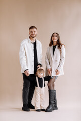 Portrait of a happy young family, with a little adorable daughter. Caring parents hold and gently hug their baby. Together they pose for a photo on beige background. Family concept.