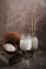 Bottle of coconut vegan milk, coco oil, whole coconut and flakes on dark background. Clean eating and healthy food concept.