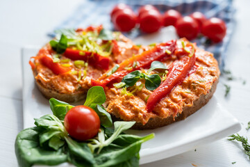vegan roasted red pepper dip sandwich spread on freshly baked bread slice with salad garnish on white porcelain plate 