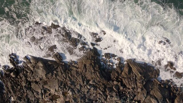 Plano a&eacute;reo zenital desde drone de mar picado con olas con mucho viento chocando contra rocas en la costa.