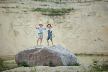 two boys in denim shorts and a hat standing on a large rock, and face off force