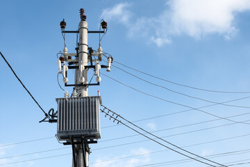 High voltage transformer mounted on a pole on blue sky background at sunny day