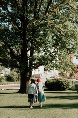 two girls are walking on green grass near a large tree