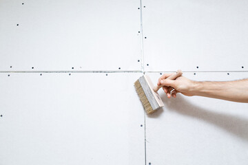 Priming the wall with a brush for renovation work. Preparing the wall before wallpapering.