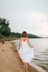 Fototapeta na wymiar a girl in a white dress walks along the sandy shore