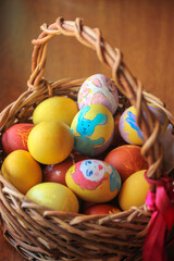 Easter wooden basket filled with colorful painted eggs on the eve of Easter. Warm background. Vertical photo.
