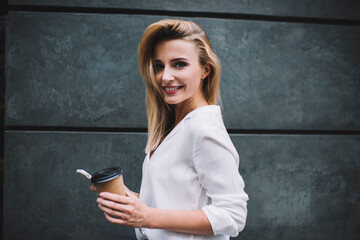 Confident young female drinking hot coffee while standing with cellphone