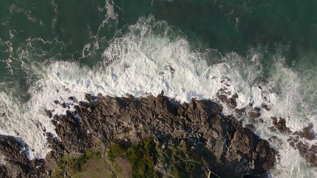 Plano a&eacute;reo zenital desde drone de mar picado con olas con mucho viento chocando contra rocas en la costa.