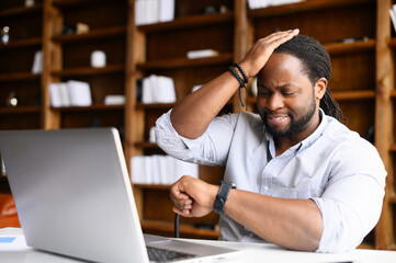 Concerned African-American young man is late, check time on a wristwatch, a sadness guy forgot about an important meeting, worried male does not have time to finish the project before the deadline