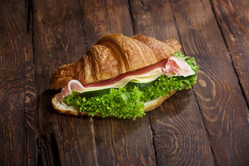 croissant sandwich with jamon, cheese, fresh cucumbers and green salad leaves on rustic wooden table, closeup