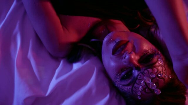 voluptuous woman with scenic makeup is lying on bed and wriggling in extasy