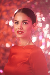 Beautiful lady in red sexy dress with make-up and elegant hairstyle. Pretty brunette woman posing against shining sequins background. Party concept. Colorful pink light