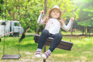 Child playing in the open playground, little happy laughing girl swinging on a swing