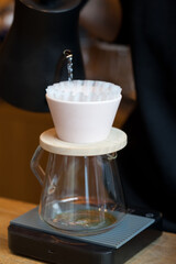 barista pouring water from kettle into pour over with paper filter on digital scales