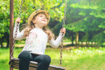 Child playing in the open playground, little happy laughing girl swinging on a swing