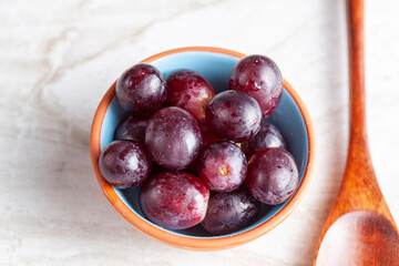 A simple image of a porcelain bowl or red grapes  and a wooden spoon on marble countertop. A concept image for vegan, raw healthy eating.