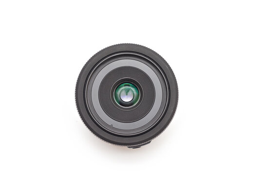 A small thin black 24 mm lens for a digital SLR camera without a name lying on a white background without covers. Top view