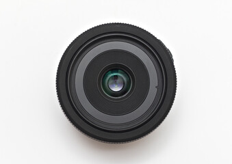 A small thin black 24 mm lens for a dSLR camera without a name lying on a white background without covers. Close-up top view