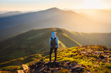 Girl on mountain peak with green grass looking at beautiful mountain valley in fog at sunset in...