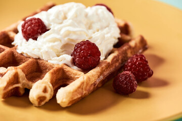 Time for dessert. Close up shot of a traditional Belgian waffle with cream cheese or ice cream and fresh raspberries on yellow plate
