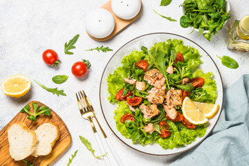 Salad with baked salmon fish. Green salad mix with tomatoes and salmon. Top view at white table.