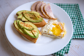 Home cooking breakfast with avocado toast, fried egg and ham on white plate