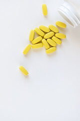 Yellow long vitamins lying next to pill jar on white background, macro, close-up, copy space. Nutritional supplements concept, health, vitamins, trendy color of 2021, Illuminating. Vertical