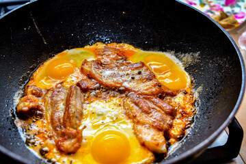 Pieces of fried bacon with eggs in a frying pan before meals.