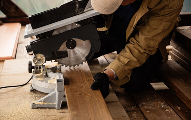Miter saw with a large metal blade in the hands of a carpenter. Working tool for sawing wooden planks. A close-up of the sawing process. Labor protection and safety rules for the use of power tools
