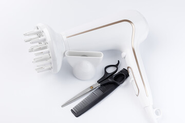 Hairdryer with different attachments, scissors, and comb on a white background.