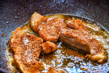 Marinated meat with spices is fried in a pan, preparing a tender and juicy pork steak.