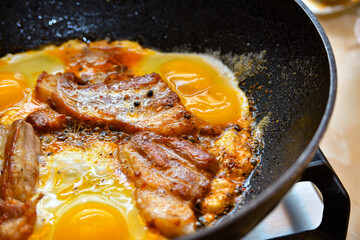 Fried meat with eggs is cooked in a pan, pork steak and chicken eggs.