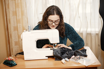Fabric in a typewriter. Woman deftly works with a sewing machine. Woman with glasses.