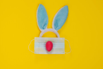 Happy Easter during the Coronavirus Time! Rabbit Blue Ears, Face Mask and Pink Egg on Yellow background.