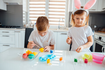 Fototapeta premium Brother and sister painting Easter eggs. Children make holiday decorations while sitting at the kitchen table