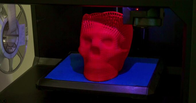 Skull printed with plastic of red color on a 3d printer. Inside 3d printer,