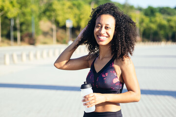 Afro runner woman smiling with a water bottle in hand