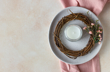 Plate with decorative spring wreath made of twigs and flowers and a candle, light concrete background. Romantic, wedding or spring table setting.
