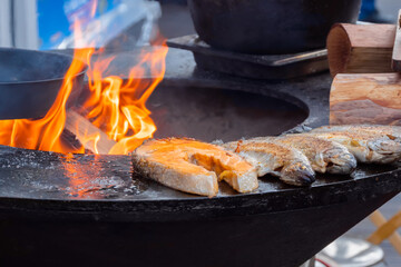 Process of grilling salmon steaks and mackerel fish on black brazier at summer local food market - close up. Outdoor cooking, barbecue, gastronomy, seafood, cookery, street food concept
