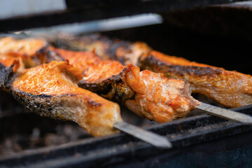 Process of cooking salmon skewers on grill over charcoal at summer local food market - close up. Outdoor cooking, barbecue, gastronomy, seafood, cookery, street food concept